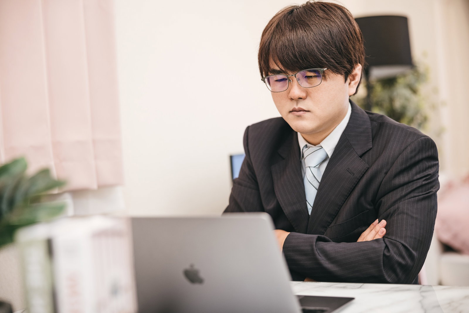ノートパソコンの前で腕を組んで悩むスーツ姿の男性会社員［モデル：はしも。］