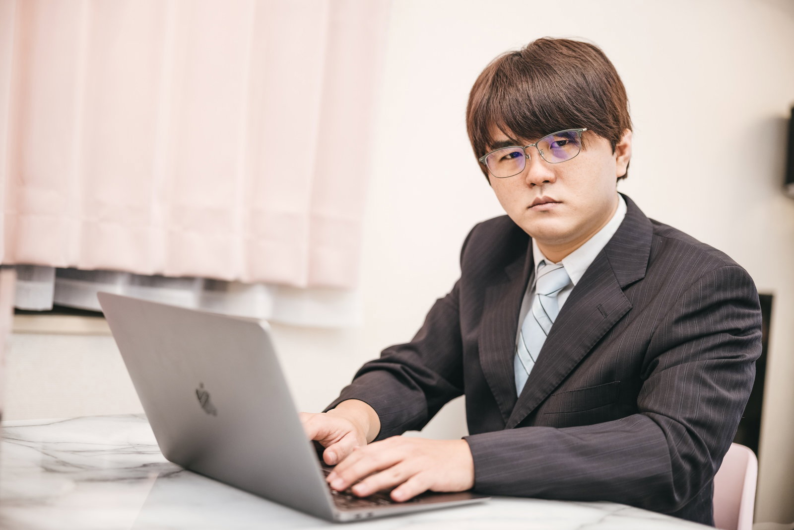デスクでノートパソコンを見つめて考え込むスーツ姿の男性会社員［モデル：はしも。］