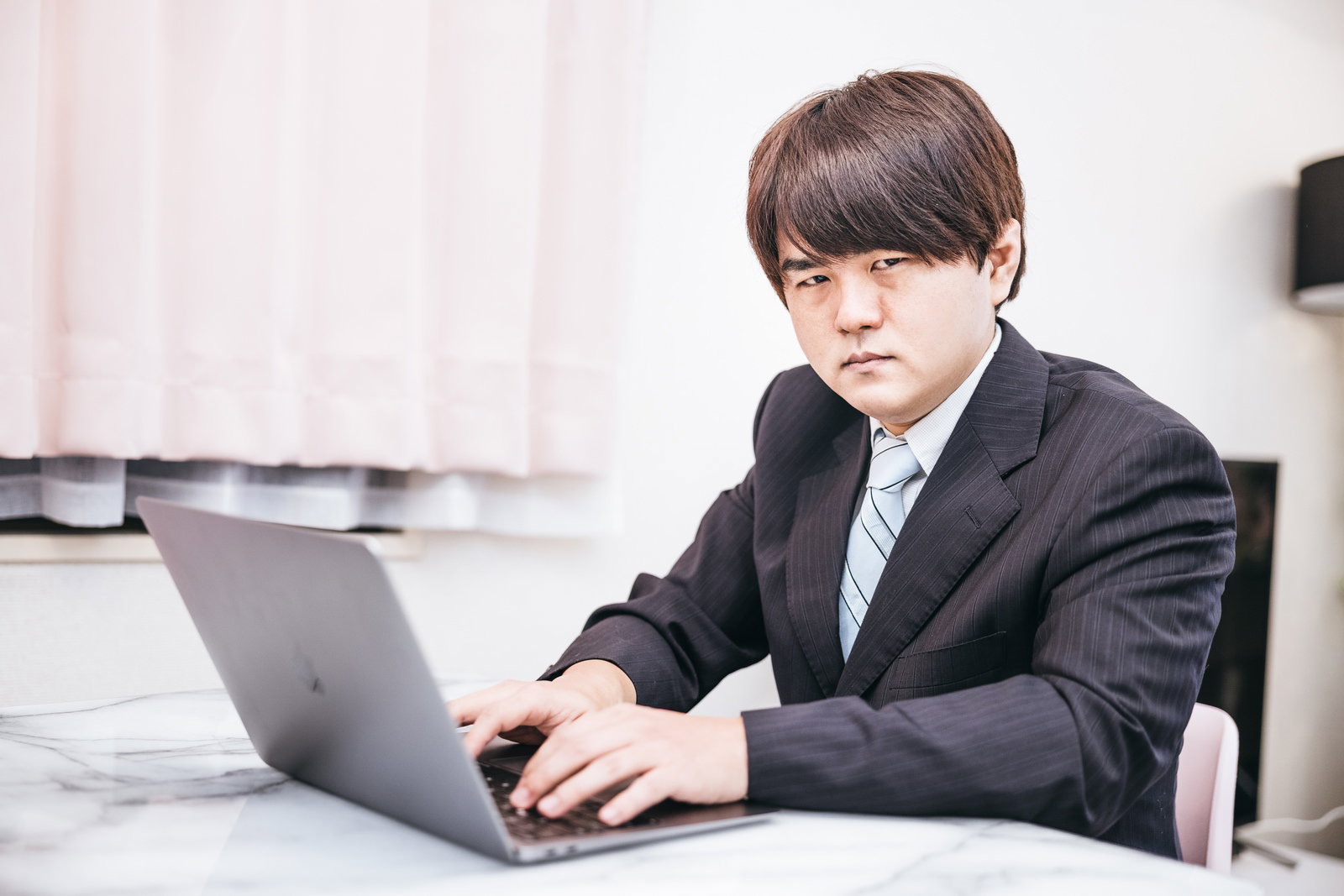 デスクでノートパソコンを使って作業するスーツを着た男性［モデル：はしも。］