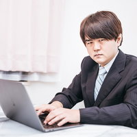 スーツ姿でノートパソコンを使いオンライン会議する男性の写真