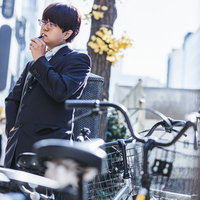 屋外の喫煙エリアで電子タバコを吸うスーツ姿の会社員の写真