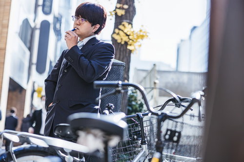 屋外の喫煙エリアで電子タバコを吸うスーツ姿の会社員