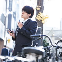 外で一服しながら次の予定をスマートフォンで確認する会社員の写真