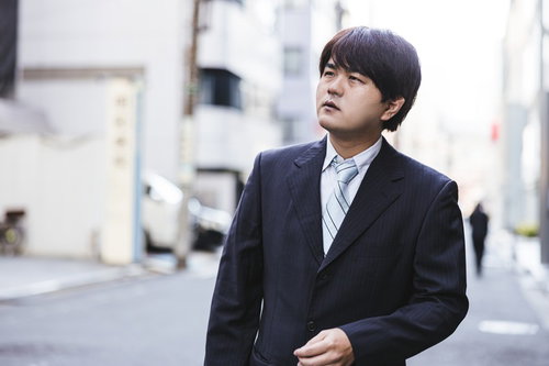 張り込みをするスーツ姿の探偵男性が街角で監視捜査