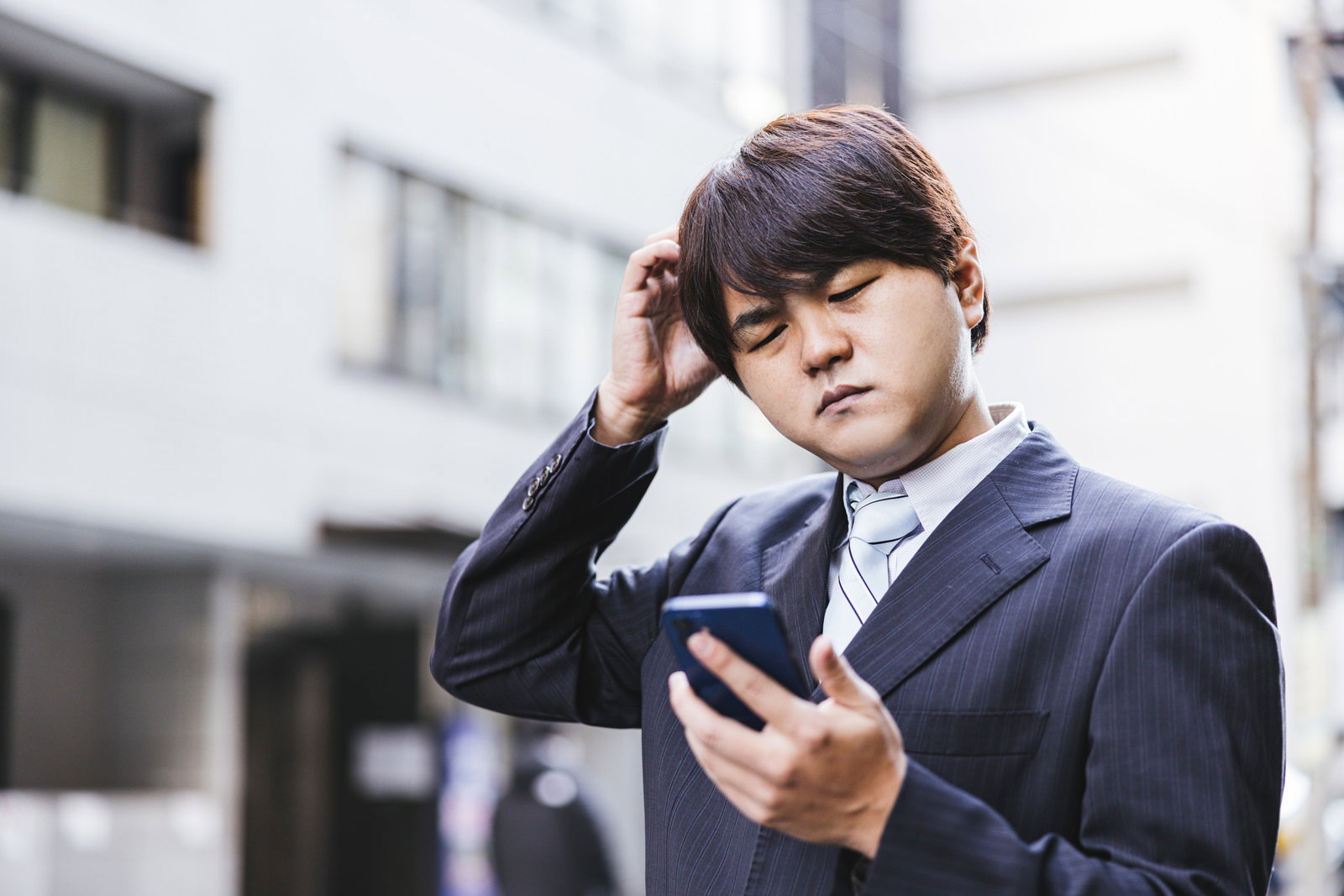 スマホを見て頭を抱えるビジネスマン［モデル：はしも。］