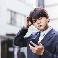 またお祈りメールかよ・・・とスマートフォンを見て頭を抱えるビジネスマンの写真