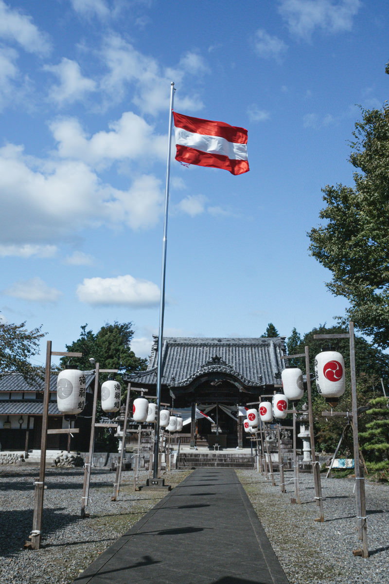 青空の下、参道に祭の旗と提灯が並ぶ白髭神社の境内風景