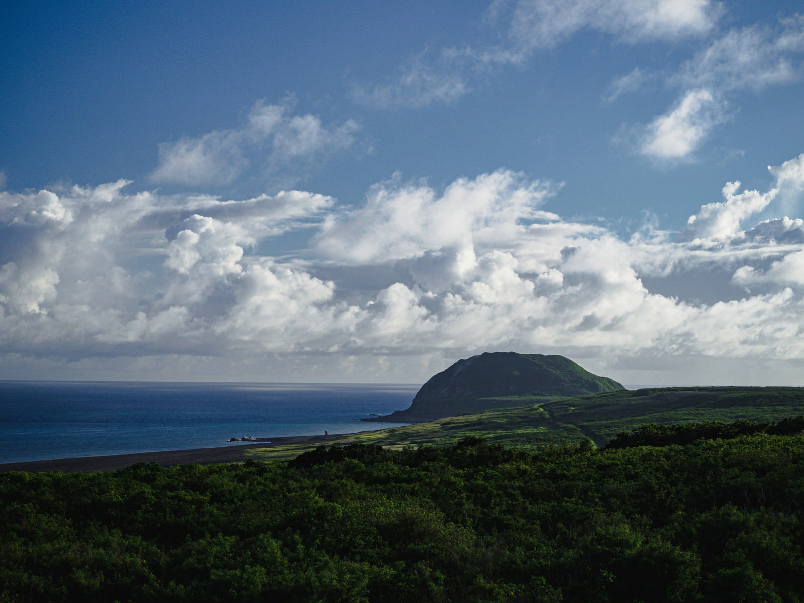 青い海と空を背景に、緑の植生に覆われた摺鉢山と翁浜海岸の風景