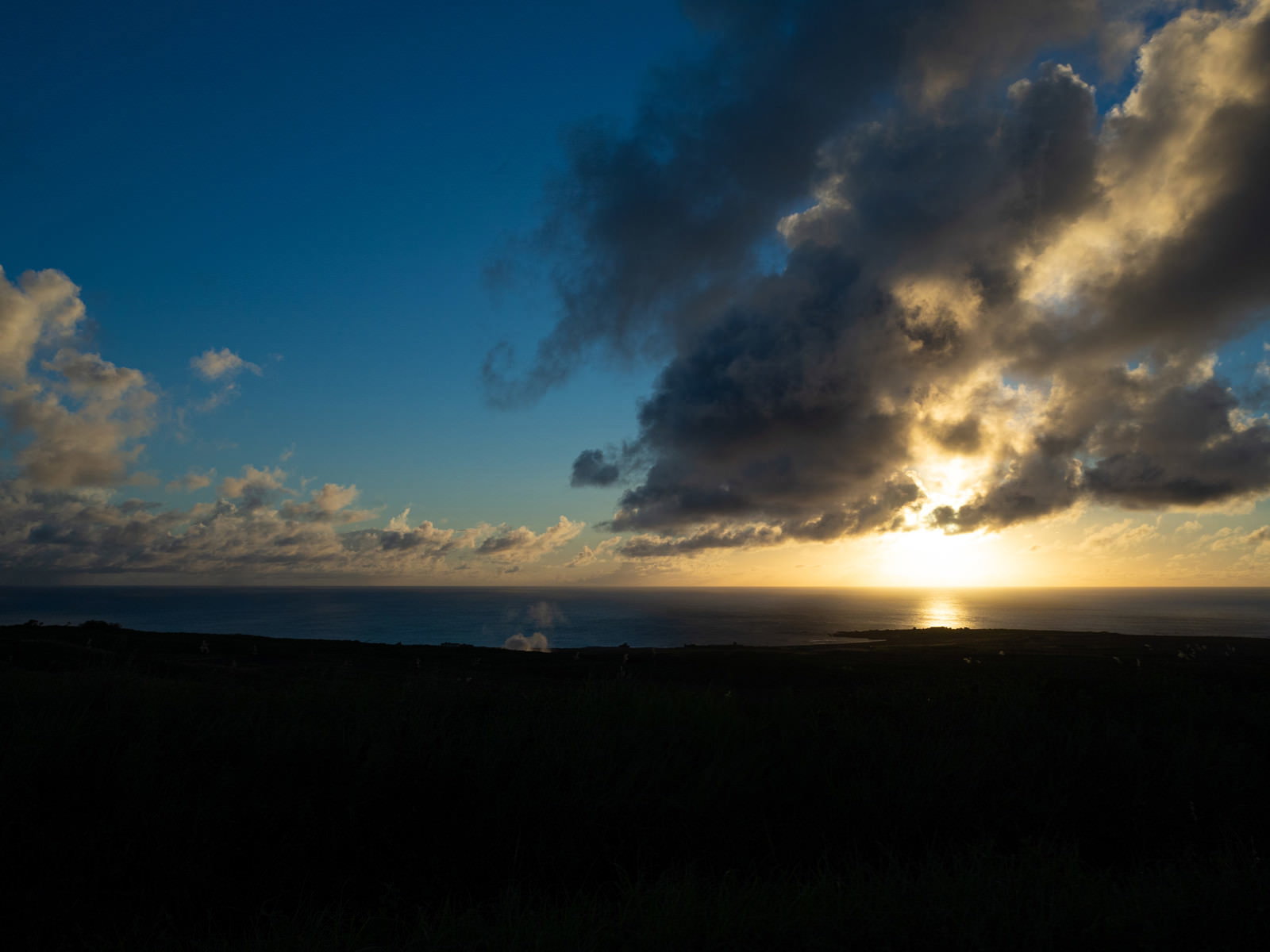 硫黄島の摺鉢山と千鳥ヶ浜の向こうに夕陽に輝く雲が見える海岸の風景