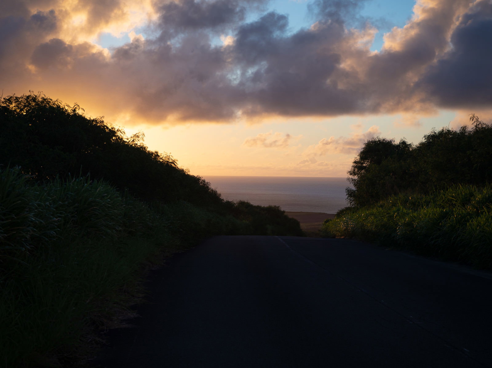 夕暮れ時の硫黄島で、オレンジ色の夕焼け空の下を一本道が奥へと続く風景