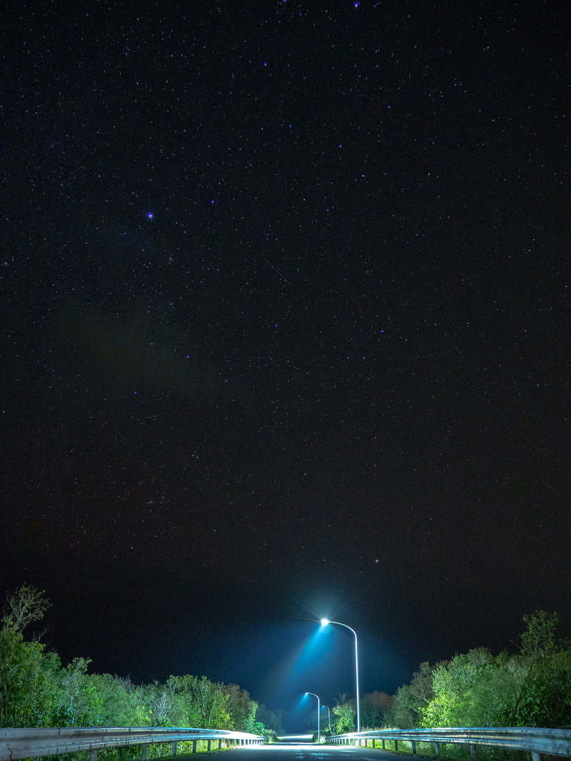街灯に照らされた夜道の向こうに満点の星空が広がる夜景