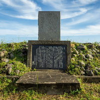 青空と雲の下に建つ日米再会の碑と石積み基台の写真