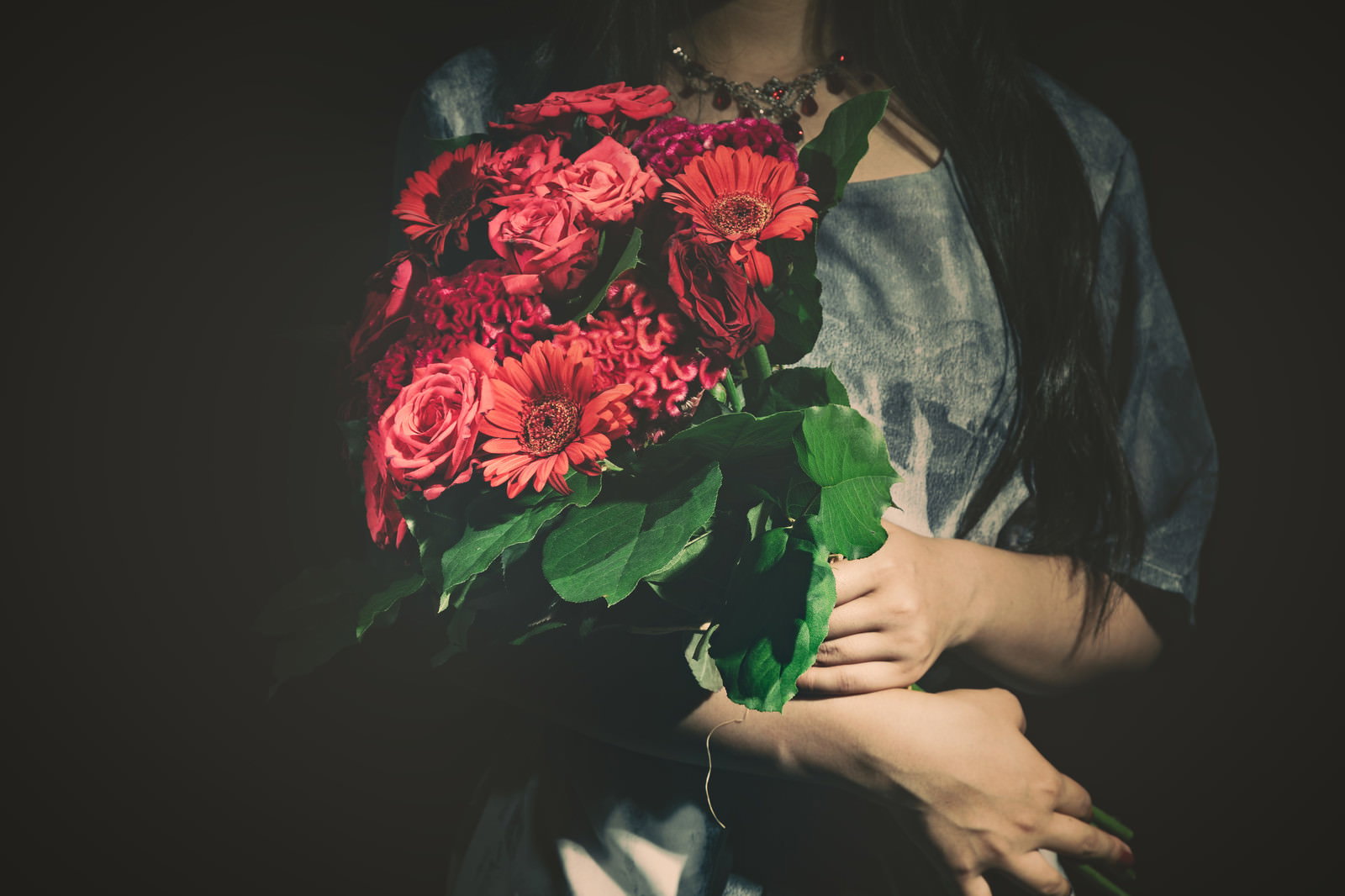 赤いバラの花束を胸元に抱える女性の暗い雰囲気の写真