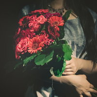 赤いバラの花束を抱えた女性の暗く深刻な表情の写真