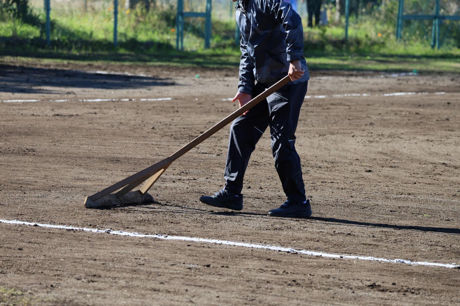 Male worker using a dragnet to level the soil on a baseball field