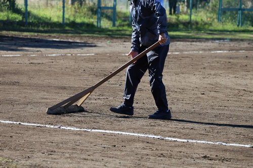 レーキを使って野球場のグラウンドを整備する作業員