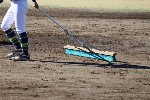 青いブラシでグラウンドの土を整備する野球場スタッフ