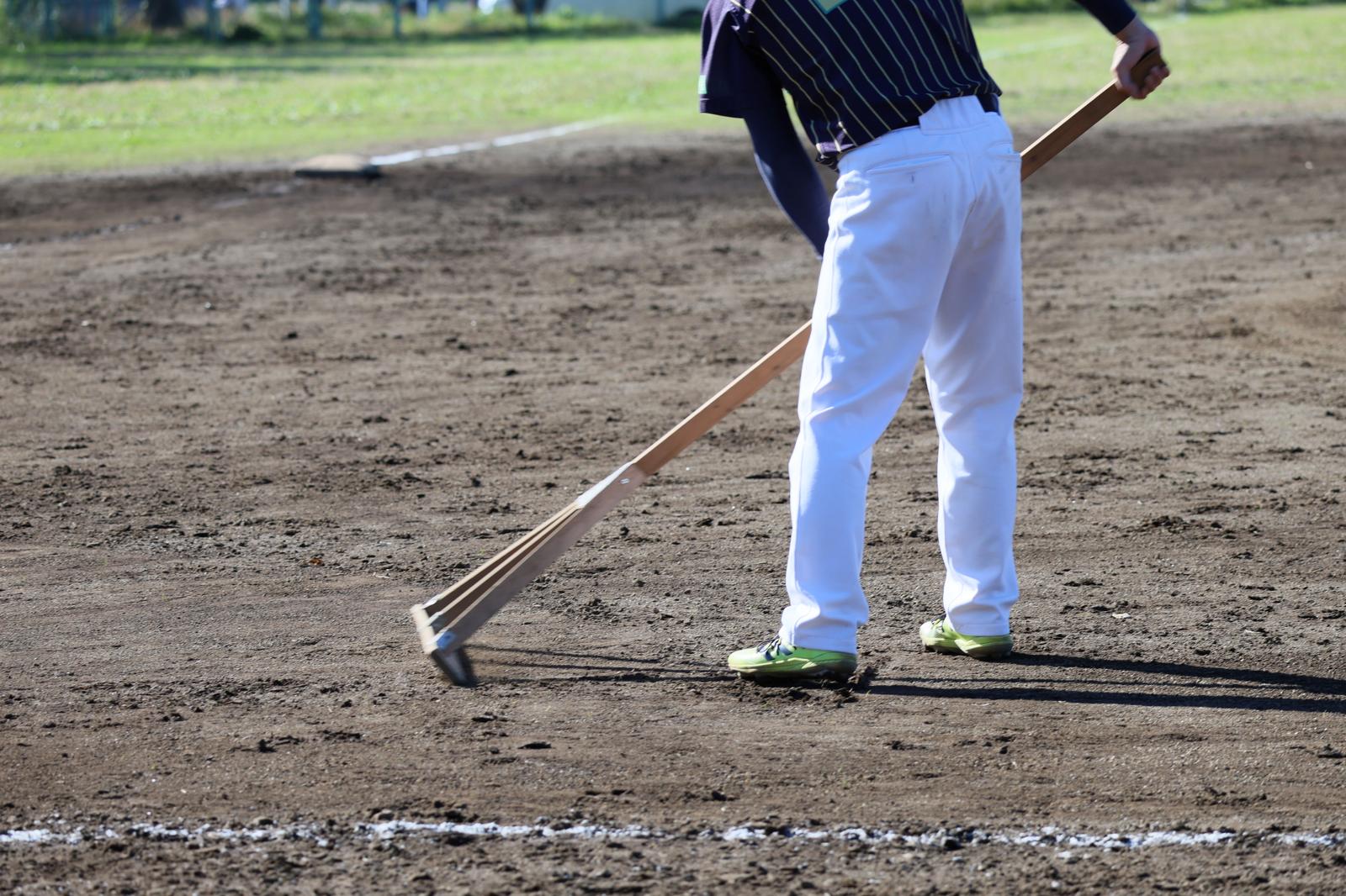 Groundskeepers using rakes to maintain the soil on a baseball field