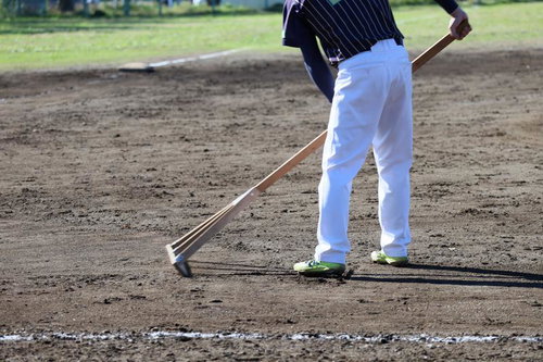 野球場でレーキを使ってグラウンドを整備する作業員の様子