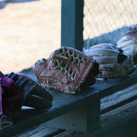 木製ベンチに並ぶキャッチャーミットとヘルメット、野球道具の写真