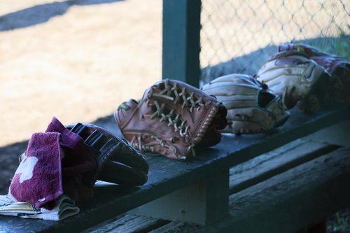木製ベンチに並ぶキャッチャーミットとヘルメット、野球道具