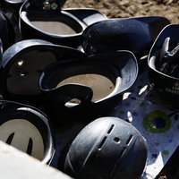 土の地面に散らばる複数の黒いバッティングヘルメットの写真