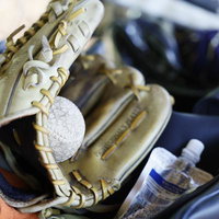 紺色のスポーツバッグに収納された茶色の革製野球グローブと白い硬式ボールの写真