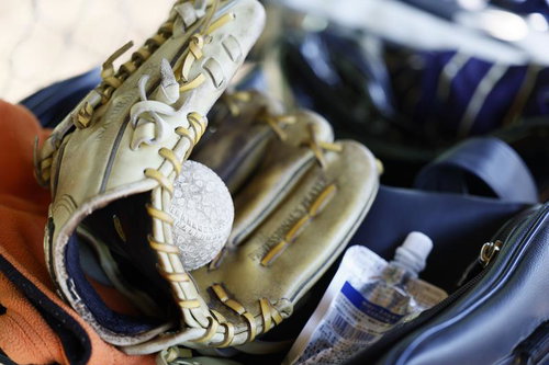 紺色のスポーツバッグに収納された茶色の革製野球グローブと白い硬式ボール