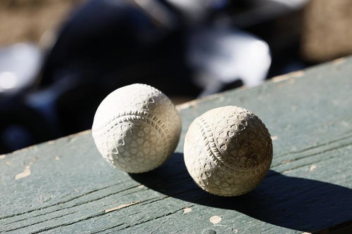 木製ベンチに並ぶ2個の野球ボール、赤い縫い目がくっきり