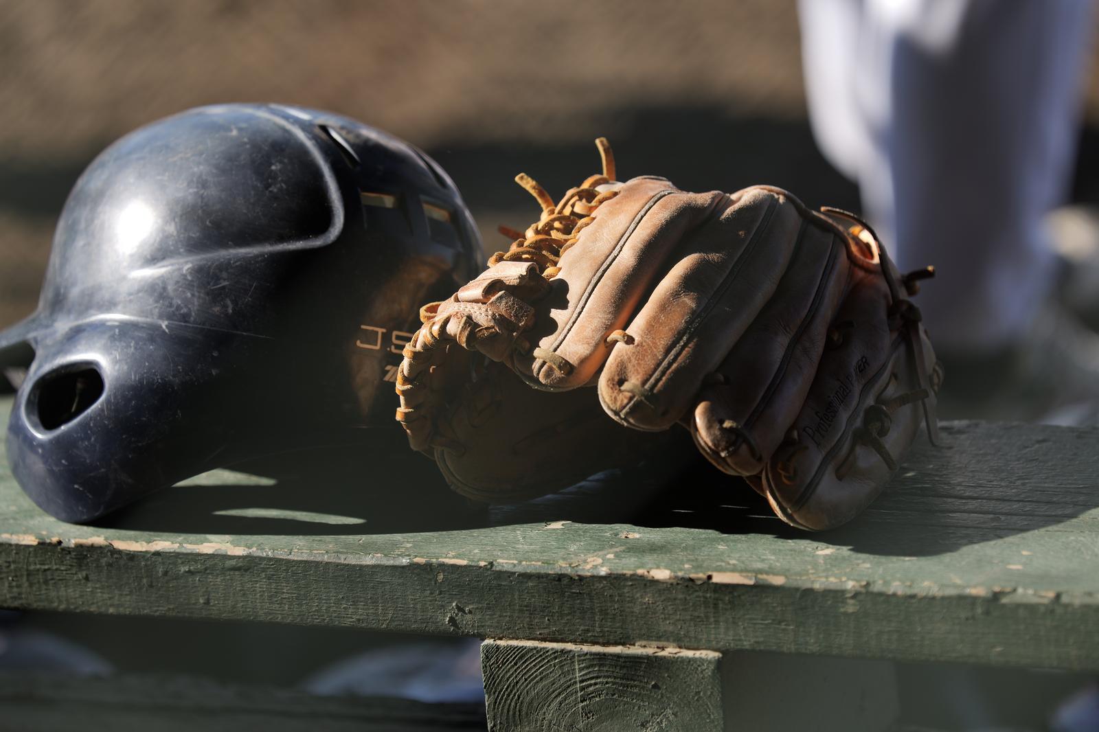 A black baseball helmet and brown glove on a wooden bench