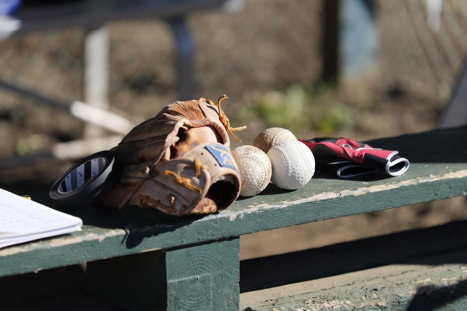 A brown baseball glove and white balls on a green bench in a park