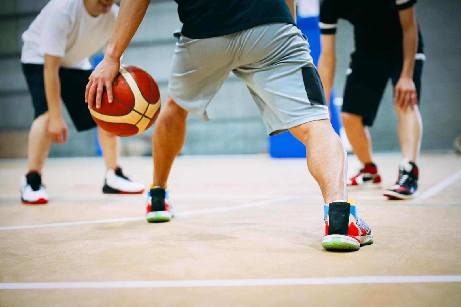 室内体育館でバスケットボールをドリブルする男性選手と周囲の選手たち