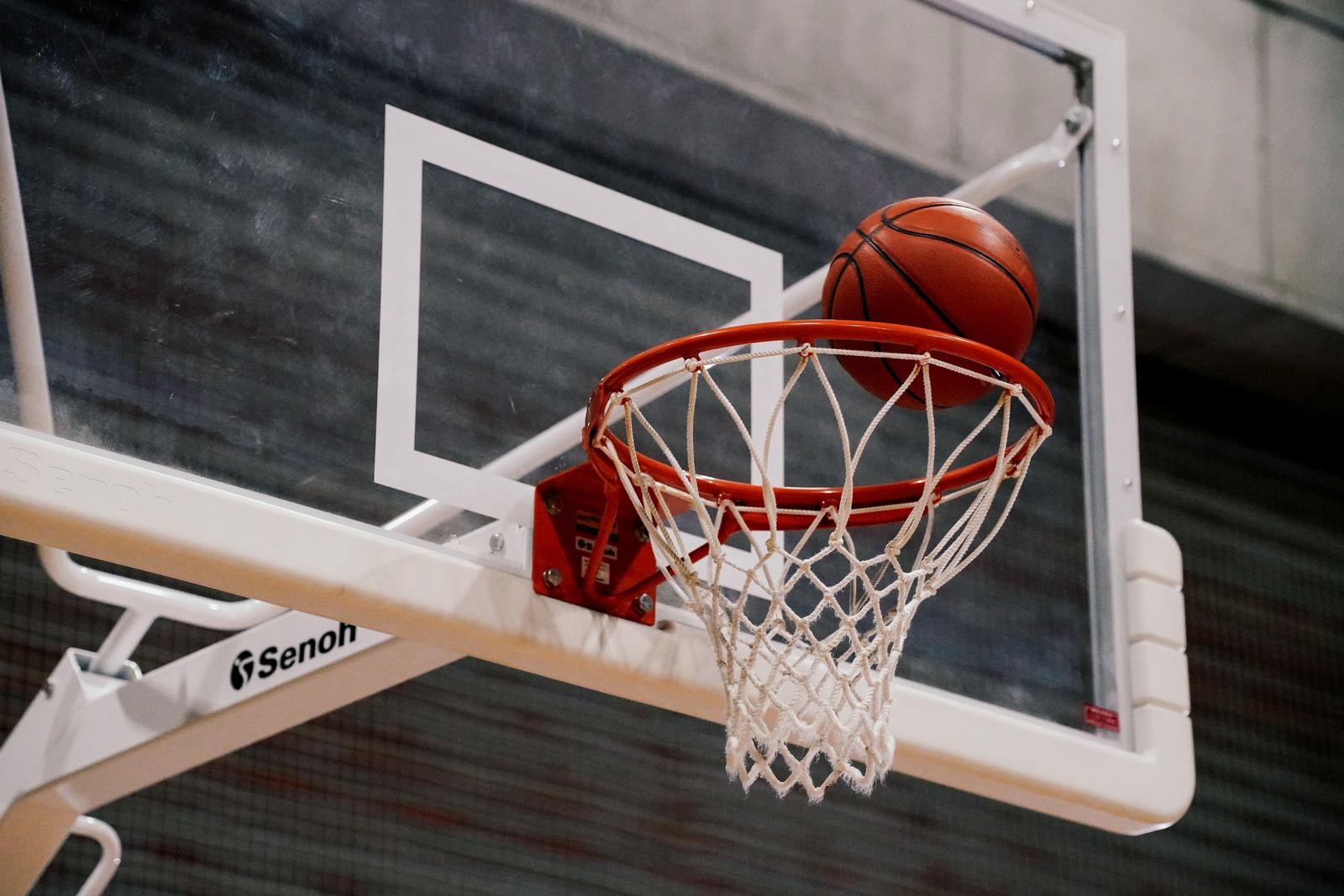 ゴールに吸い込まれるバスケットボール。赤いボールがリングに乗っている