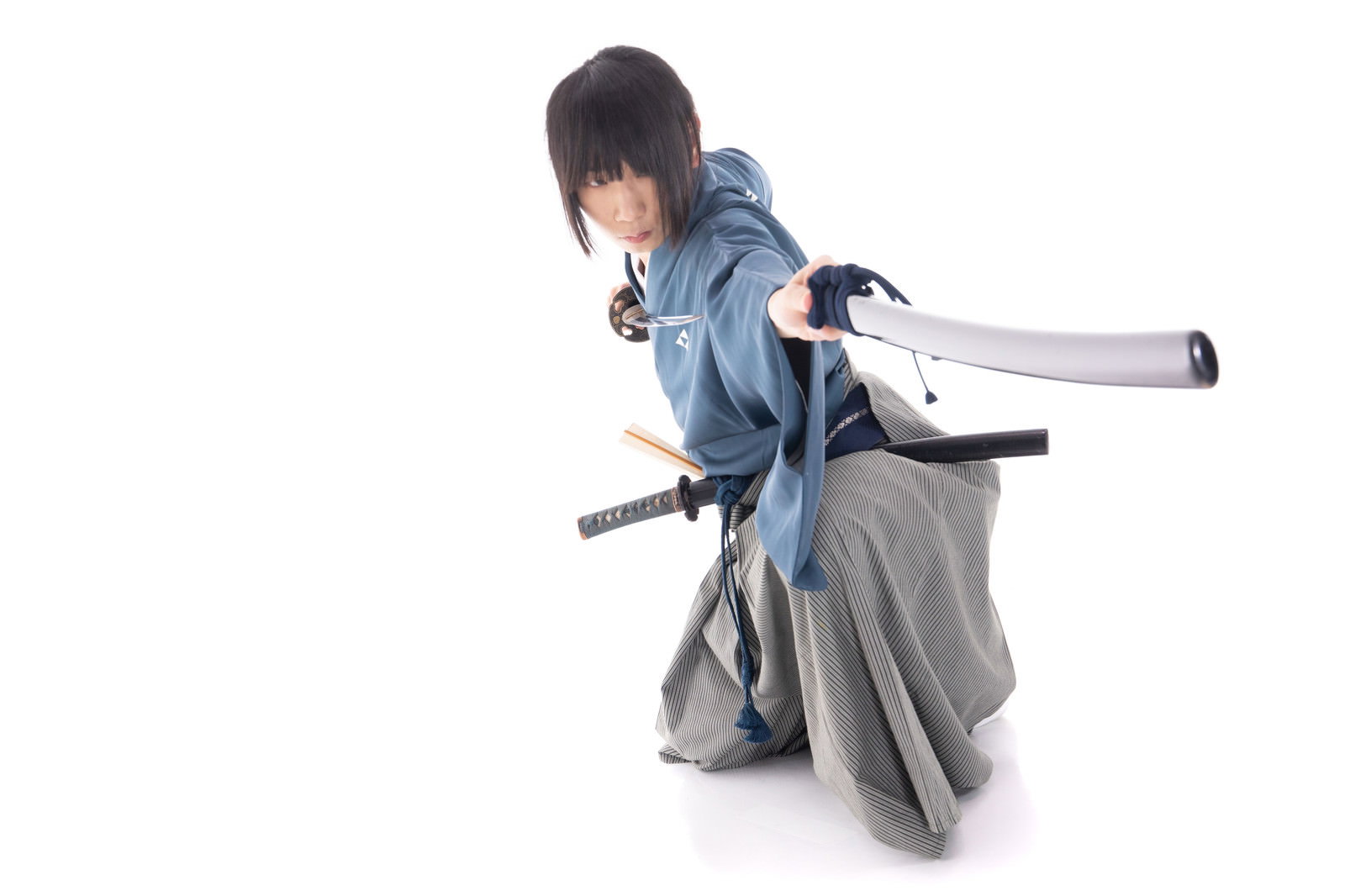 袴を着た男性が白背景で刀の鞘を使った攻撃動作をしている［モデル：まーこ］