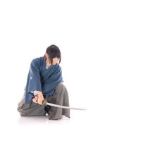 紺色の着物姿でしゃがみながら日本刀を構える侍の写真