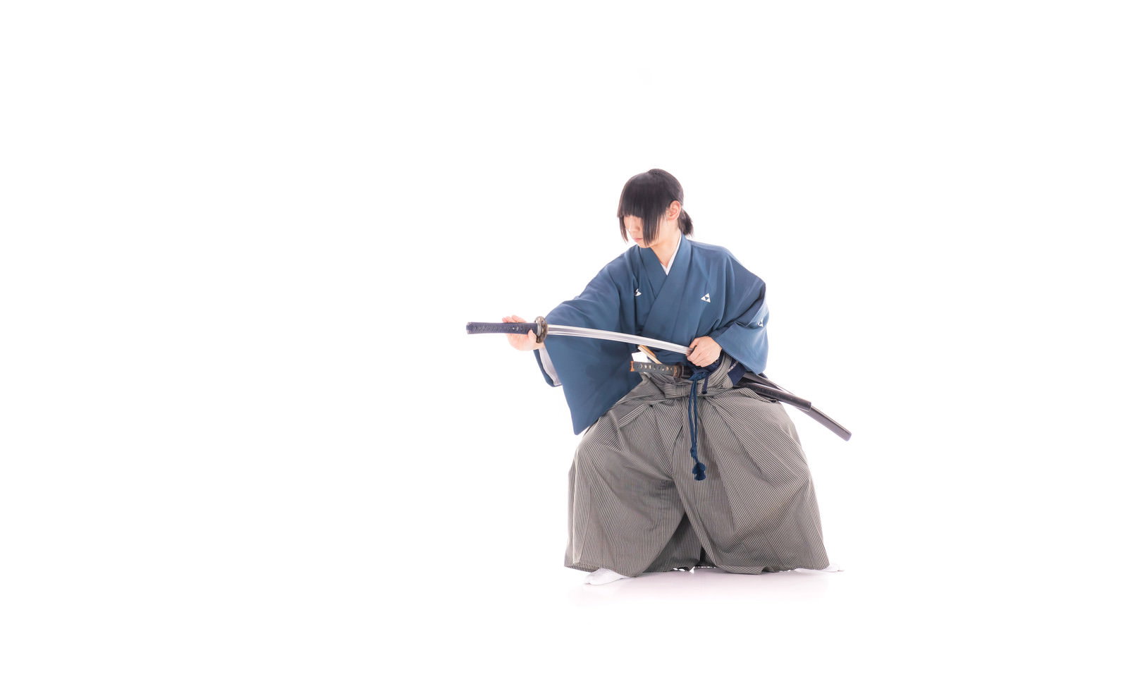 白い背景で紺色の袴を着た侍が刀を鞘に納刀している様子［モデル：まーこ］
