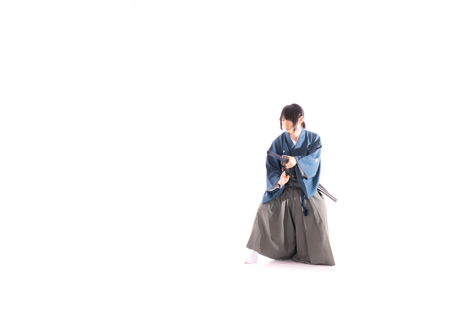 青い着物を着た武士が腰の日本刀に手をかけて抜刀しようとしている様子［モデル：まーこ］