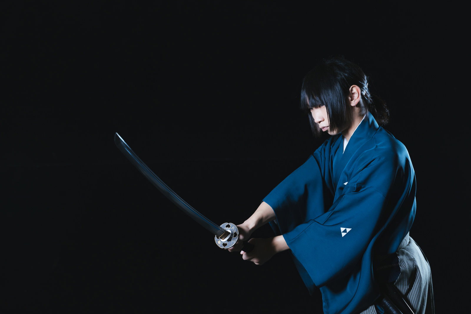 暗闇の中で日本刀を構える青い袴姿の侍［モデル：まーこ］