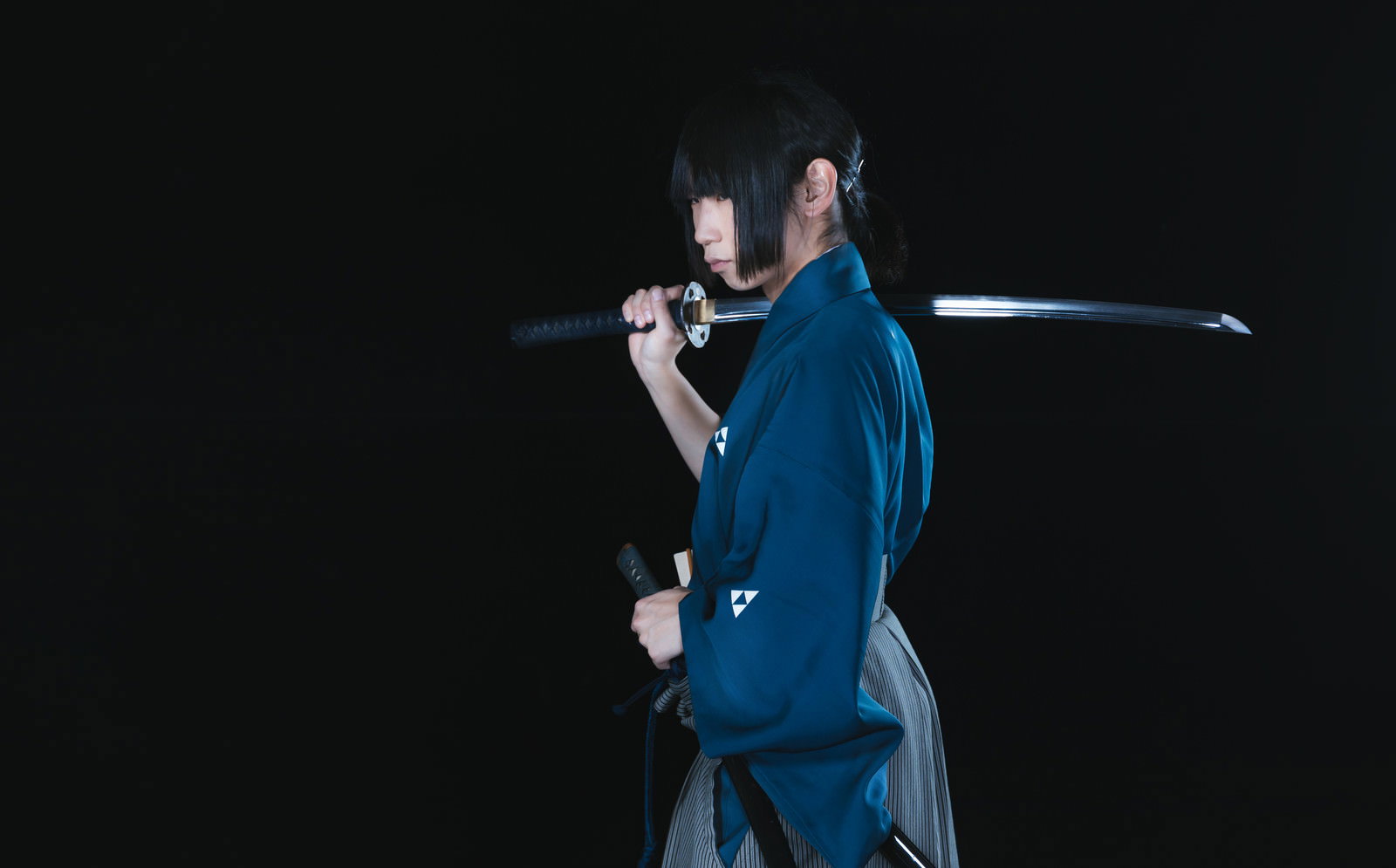 暗い背景で青い袴を着た侍が日本刀を抜刀している様子［モデル：まーこ］