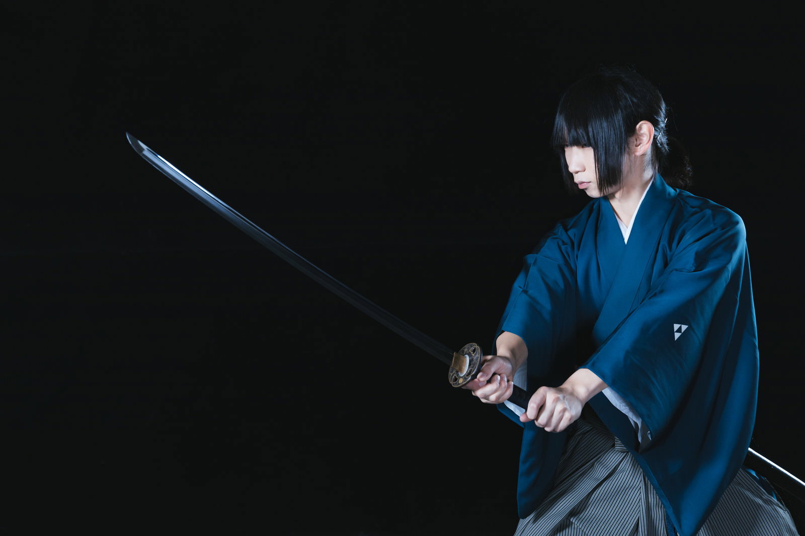 暗闇の中で日本刀を抜く紺色の着物を着た侍の男性［モデル：まーこ］