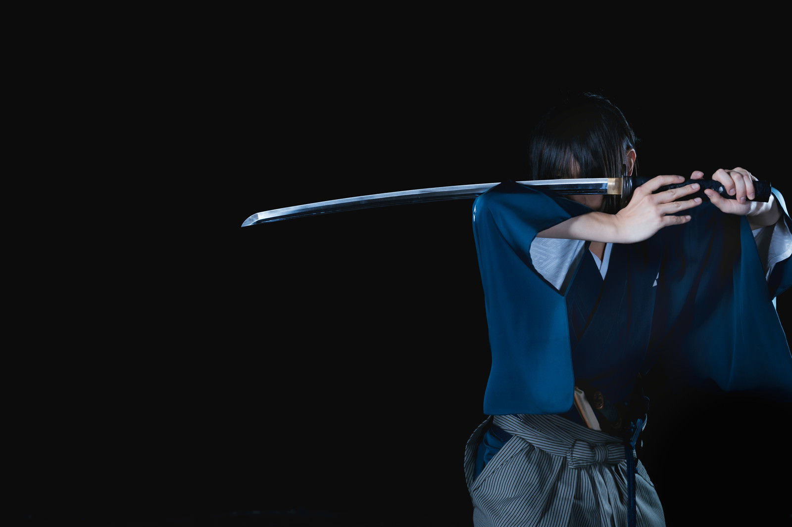 黒い背景で青い袴を着た侍が刀を抜いて構えている様子［モデル：まーこ］