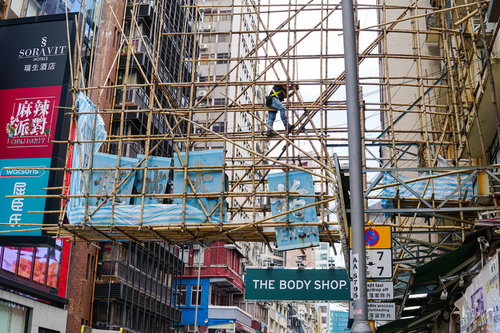香港の道路を跨ぐ竹足場と青い工事看板の建築現場風景