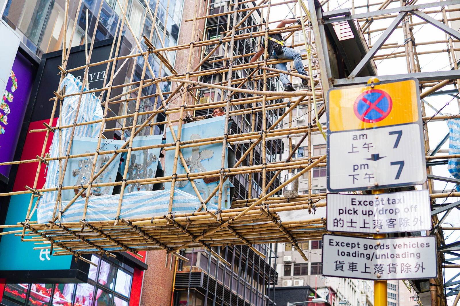 香港の街中で竹足場を組む職人の様子とカラフルな看板群