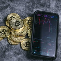 スマホのチャート画面とビットコイン、下降トレンドの写真