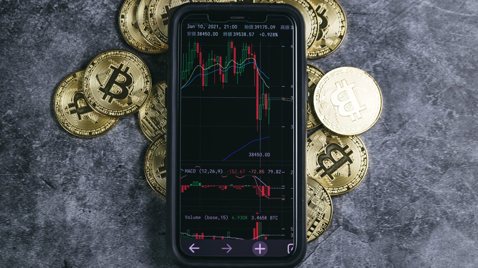 金色のビットコインコインの上に置かれた暴落チャートを表示するスマートフォン