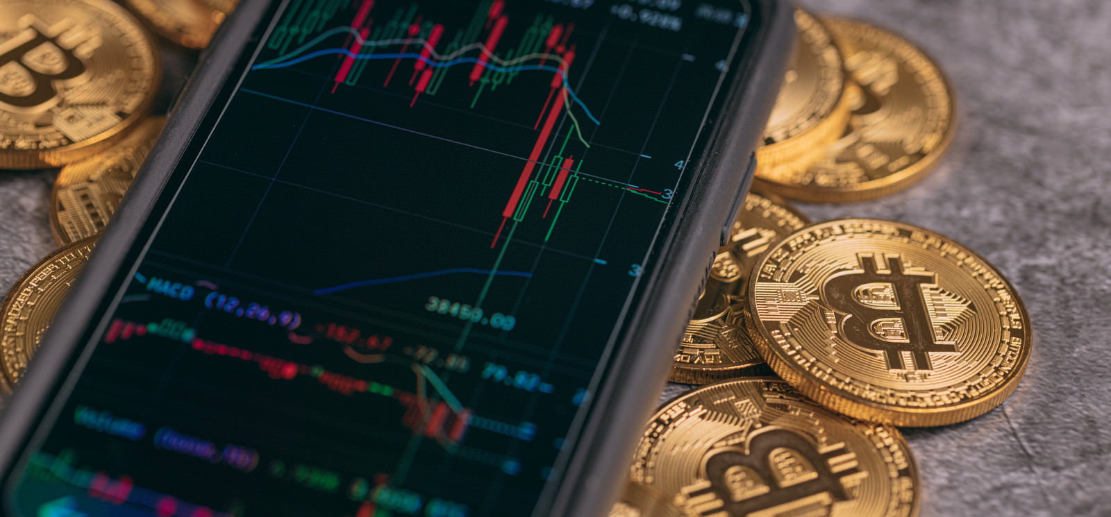 スマートフォンの画面にチャートが表示され、周りにビットコインのコインが配置されている
