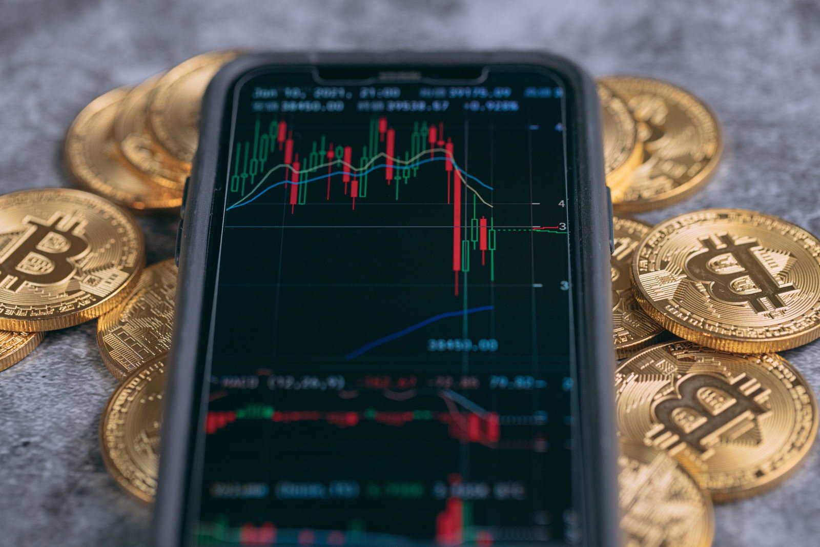 スマートフォンのチャート画面と周囲に配置されたビットコイン