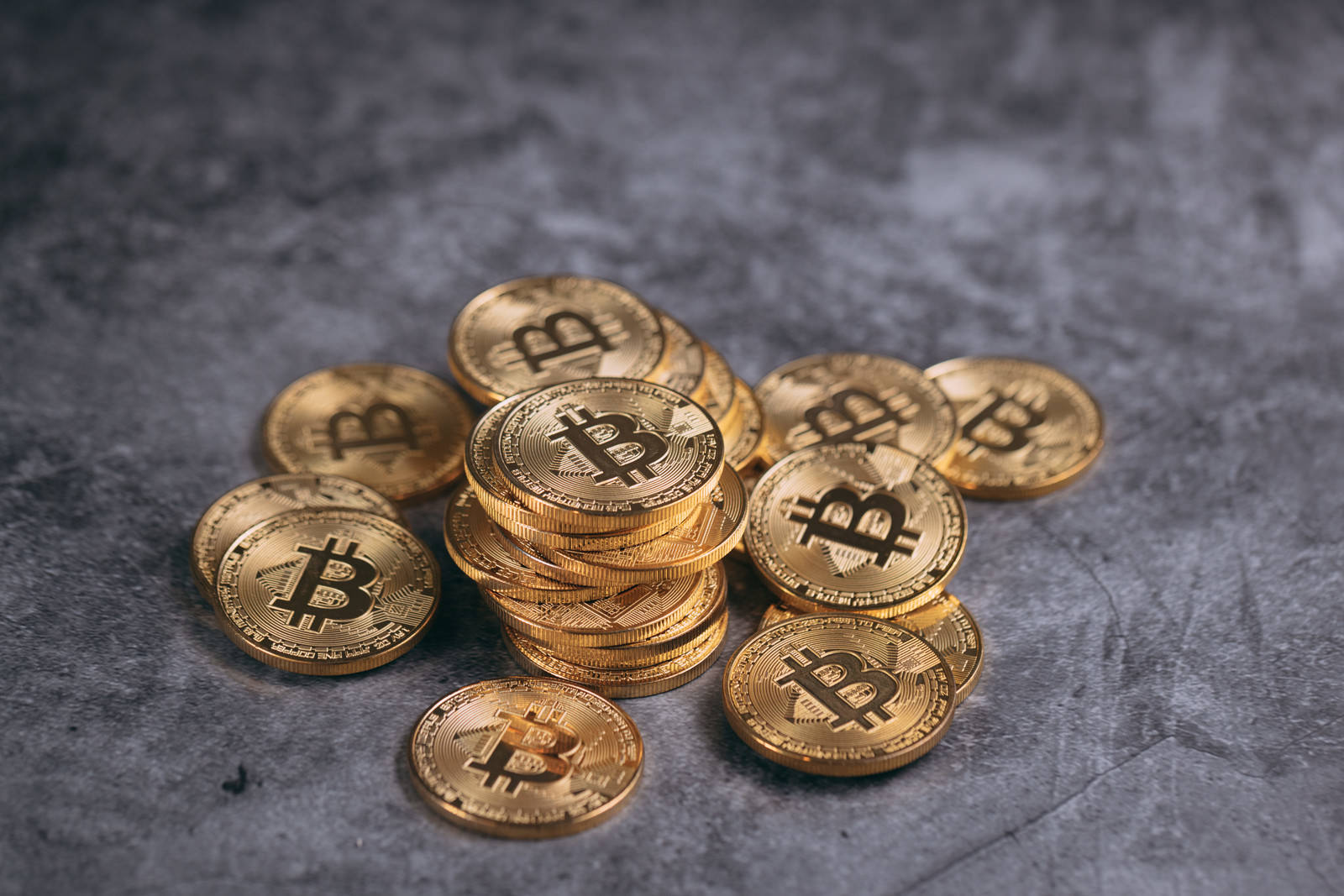 灰色の背景に金色のビットコインが複数枚積み重ねられている
