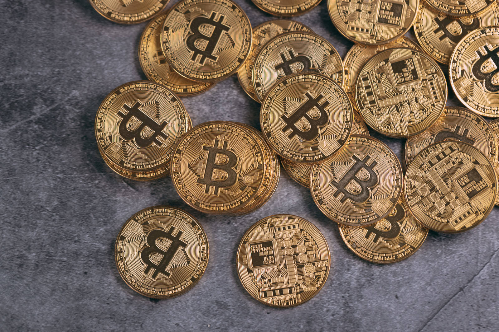 グレーの背景に金色のビットコインが複数散らばって配置された様子