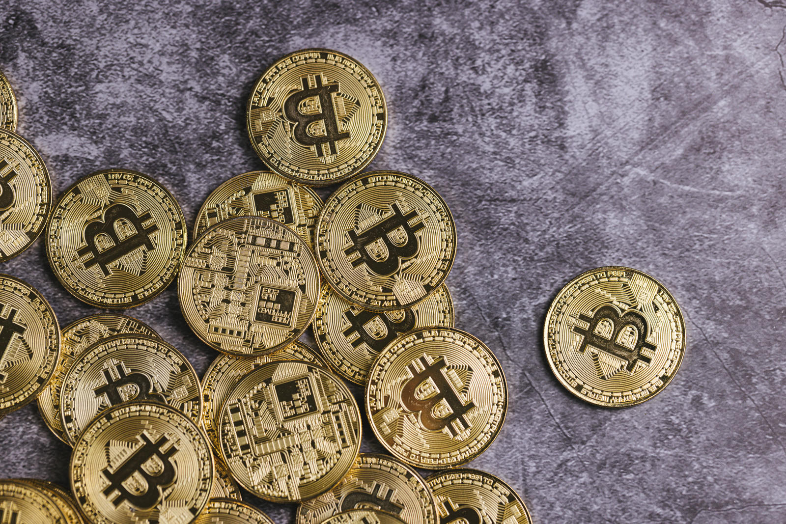 グレーの背景に金色のビットコインが裏表に散らばっている